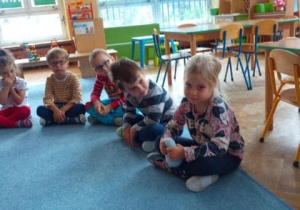 Dzieci siedzą na dywanie, dziewczynki opowiadają czego można życzyć chłopcom